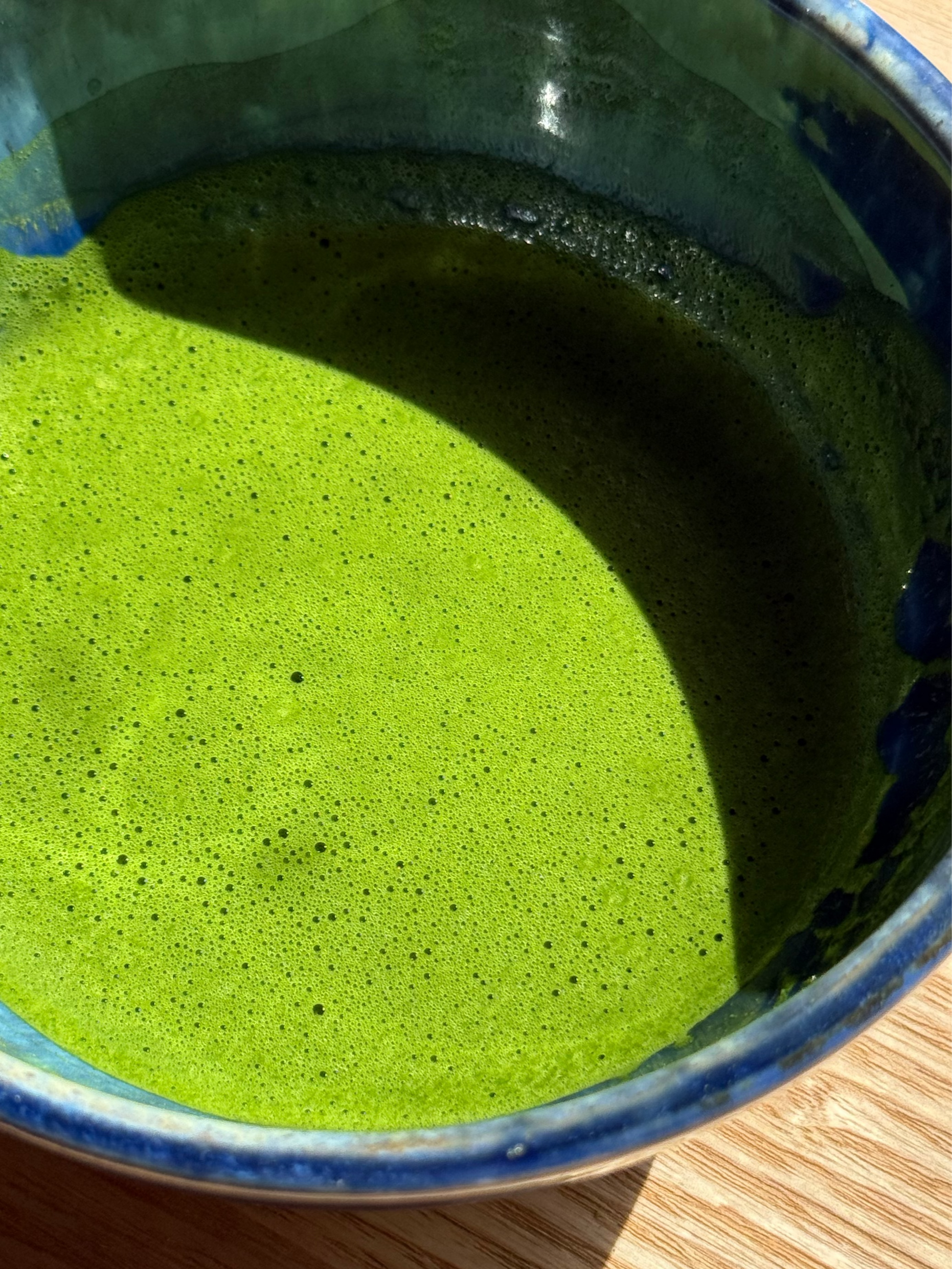 Green vibrant matcha in a blue-rimmed ceramic bowl on a wooden surface