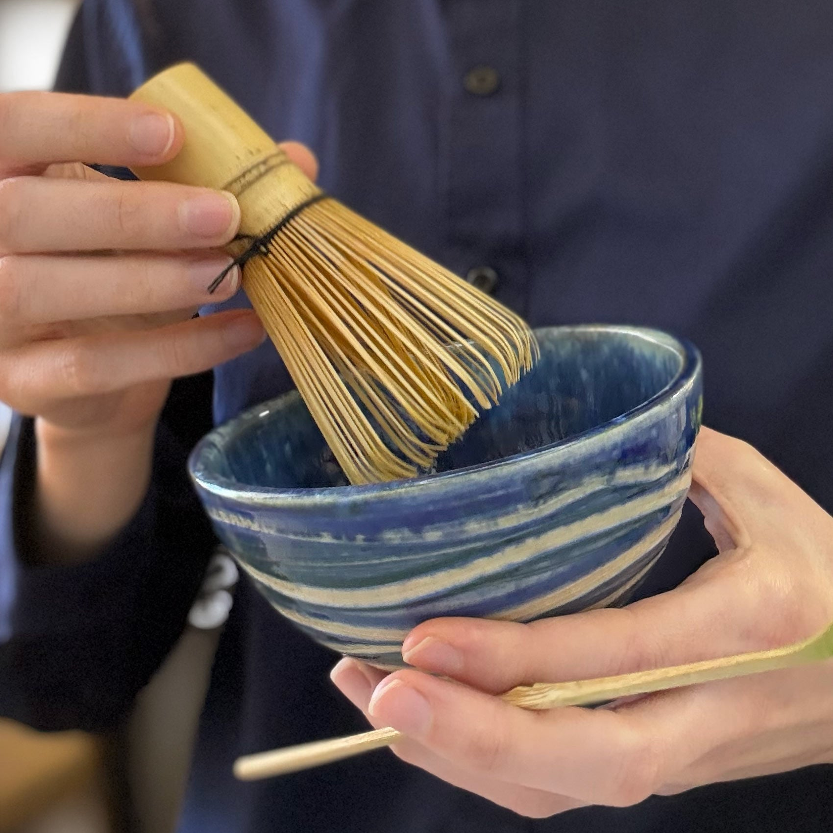 Person holding a ceramic bowl and a bamboo whisk